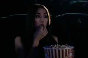 A girl in suspense in a movie theater eating popcorn.